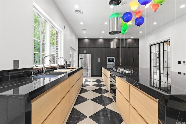 kitchen with pendant lighting, sink, light brown cabinets, and stainless steel fridge