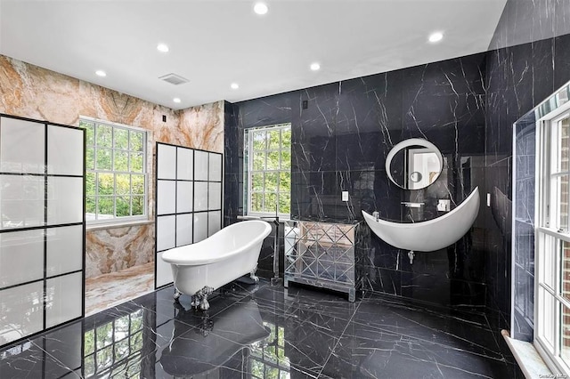 bathroom with tile walls, a tub to relax in, and plenty of natural light