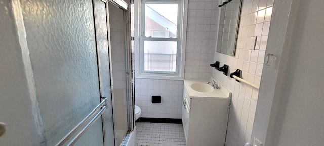 bathroom featuring vanity, a shower with door, tile patterned floors, toilet, and tile walls