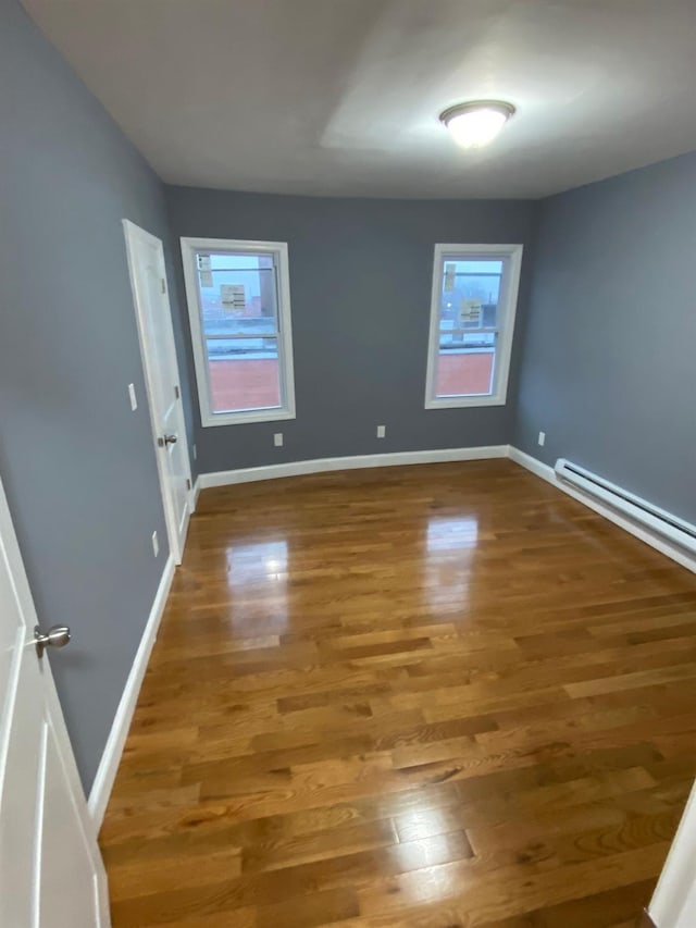 empty room with wood-type flooring and a baseboard heating unit