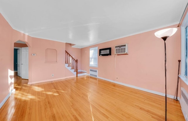 unfurnished living room with hardwood / wood-style flooring, a wall unit AC, ornamental molding, and radiator