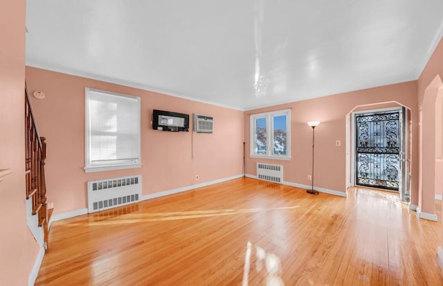 unfurnished living room with hardwood / wood-style floors, a wall mounted air conditioner, and radiator