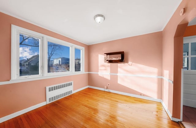 unfurnished room featuring wood-type flooring, radiator, and crown molding