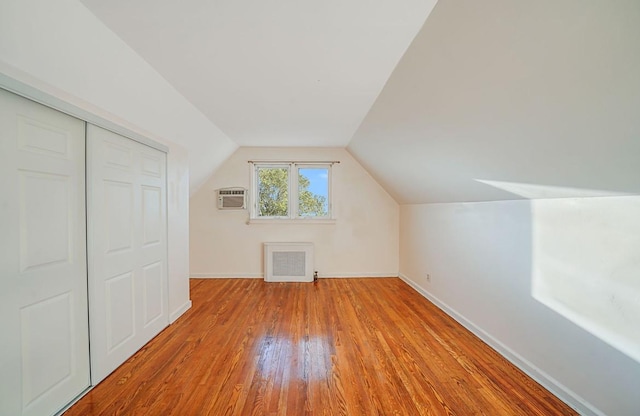 bonus room featuring a wall mounted AC, light hardwood / wood-style flooring, vaulted ceiling, and radiator heating unit