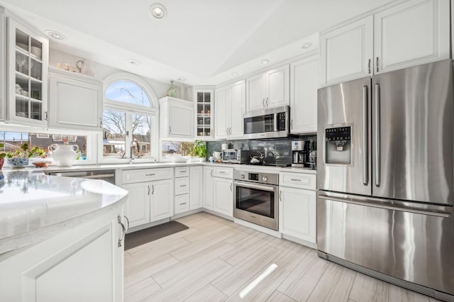 kitchen featuring vaulted ceiling, white cabinetry, appliances with stainless steel finishes, and decorative backsplash