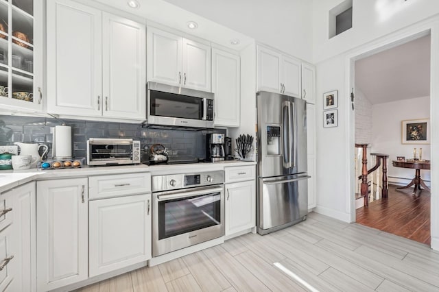 kitchen with appliances with stainless steel finishes, a baseboard heating unit, white cabinets, light hardwood / wood-style floors, and backsplash