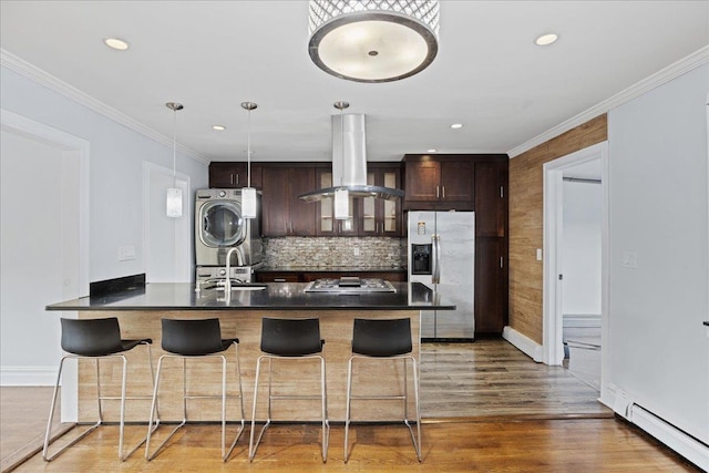 kitchen with a breakfast bar, stainless steel appliances, island range hood, sink, and stacked washer and dryer