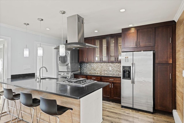 kitchen featuring sink, stacked washing maching and dryer, island range hood, appliances with stainless steel finishes, and light wood-type flooring