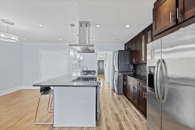 kitchen featuring decorative light fixtures, stacked washer / dryer, stainless steel appliances, and an island with sink