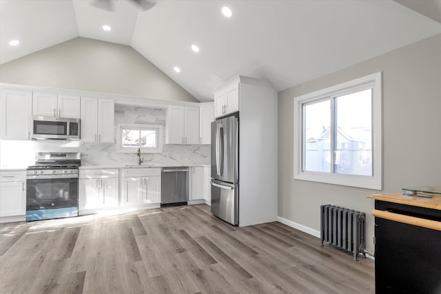 kitchen with a wealth of natural light, stainless steel appliances, radiator heating unit, light hardwood / wood-style floors, and white cabinetry