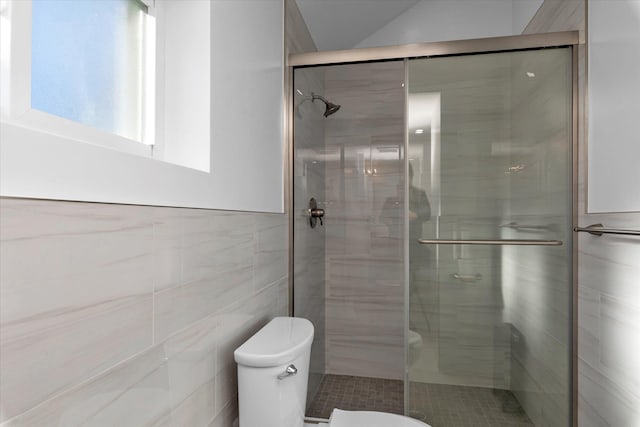 bathroom featuring toilet, a shower with door, and tile walls