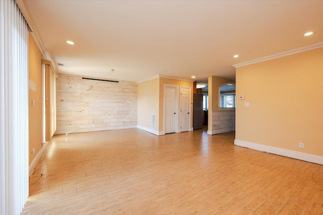 empty room with light wood-type flooring, crown molding, and wooden walls