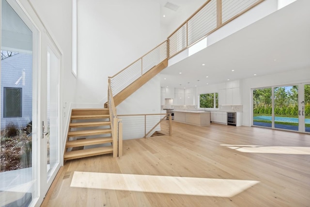 stairs featuring wine cooler, a towering ceiling, and wood-type flooring