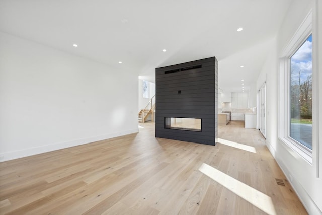 unfurnished living room with a multi sided fireplace and light hardwood / wood-style flooring