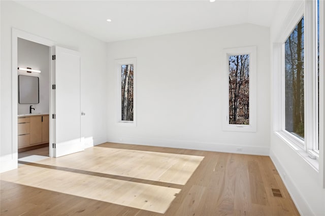 unfurnished bedroom with lofted ceiling, ensuite bathroom, light hardwood / wood-style floors, and sink