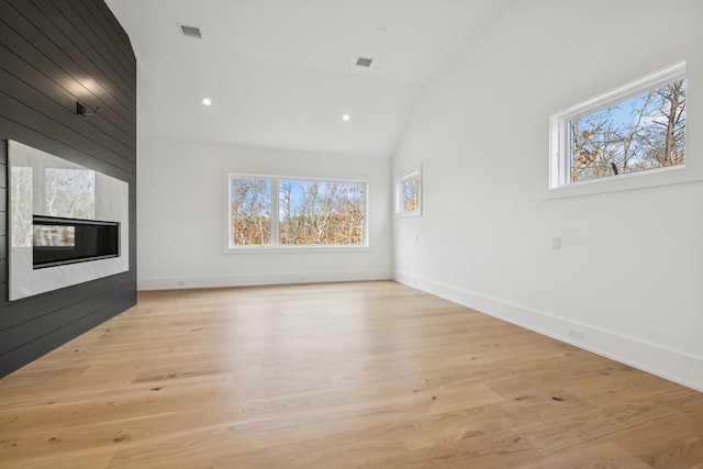 unfurnished living room featuring plenty of natural light, a large fireplace, light wood-type flooring, and lofted ceiling