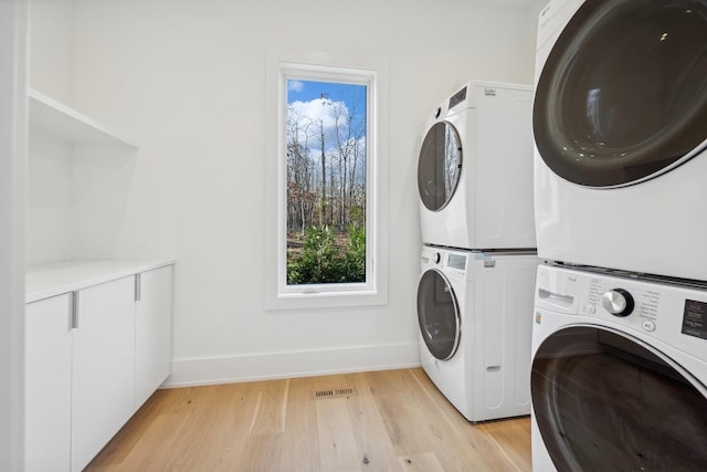 washroom with stacked washer / drying machine and light hardwood / wood-style flooring