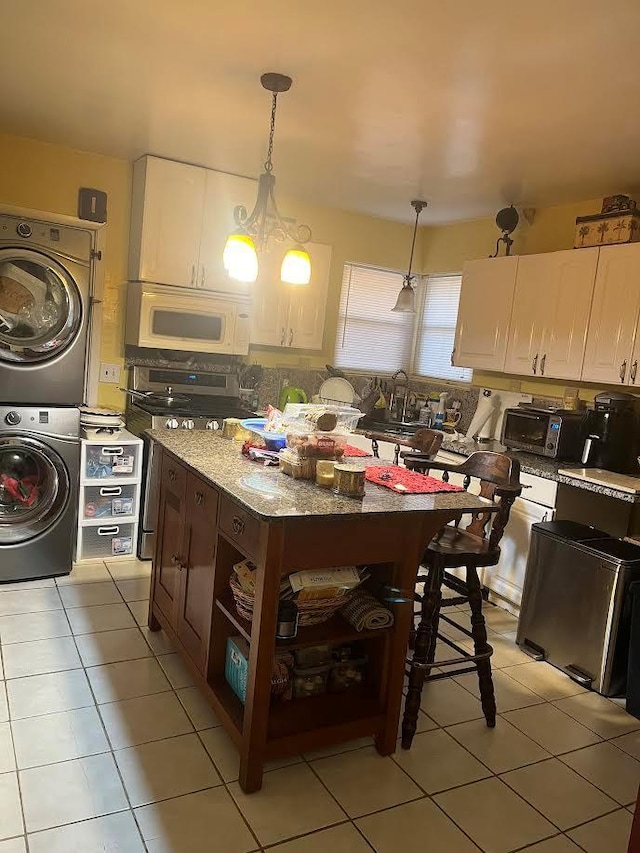 kitchen with stainless steel range, white cabinets, pendant lighting, and stacked washer and clothes dryer