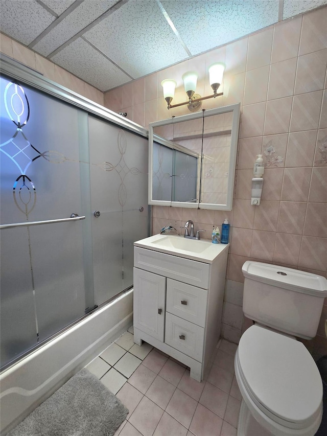 full bathroom featuring combined bath / shower with glass door, vanity, tile walls, tile patterned flooring, and toilet