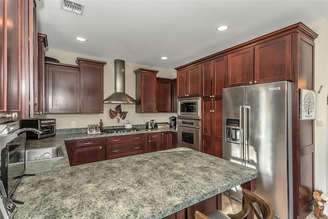 kitchen featuring sink, stainless steel appliances, wall chimney range hood, a kitchen breakfast bar, and tile patterned floors