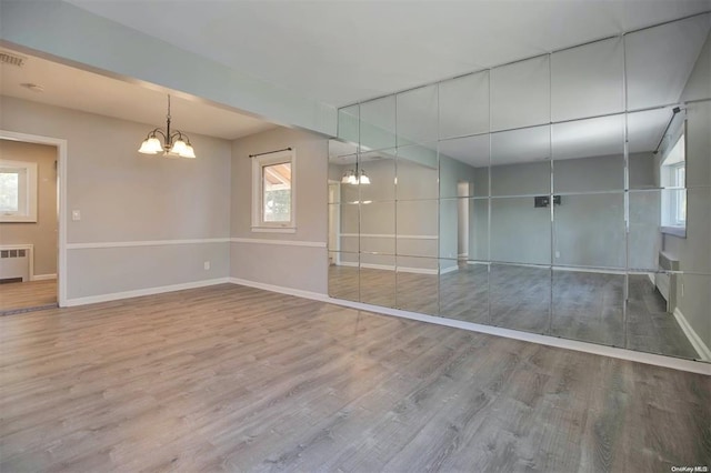 unfurnished room with hardwood / wood-style flooring, radiator, and a chandelier