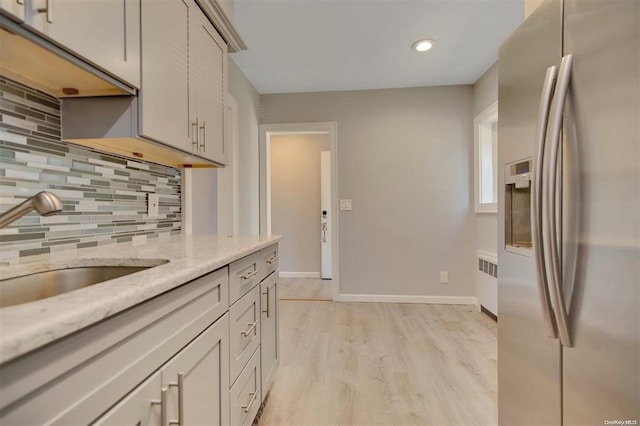 kitchen featuring stainless steel fridge, light wood-type flooring, tasteful backsplash, sink, and radiator heating unit