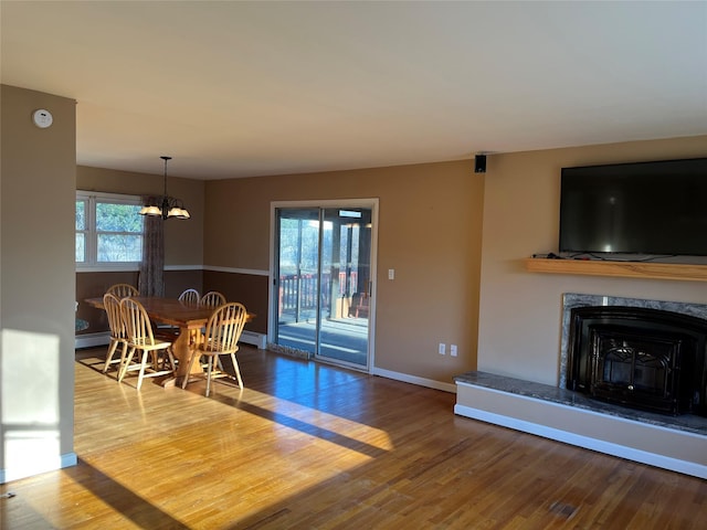 dining room featuring wood-type flooring, a baseboard radiator, a notable chandelier, and a premium fireplace