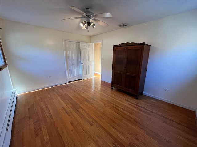 unfurnished bedroom with baseboard heating, a closet, ceiling fan, and dark hardwood / wood-style flooring