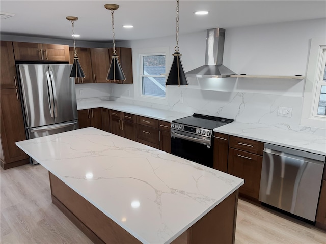 kitchen featuring decorative backsplash, stainless steel appliances, wall chimney range hood, pendant lighting, and light hardwood / wood-style flooring