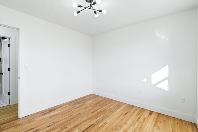 spare room with wood-type flooring and an inviting chandelier