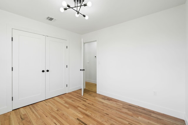 unfurnished bedroom featuring light hardwood / wood-style floors, an inviting chandelier, and a closet