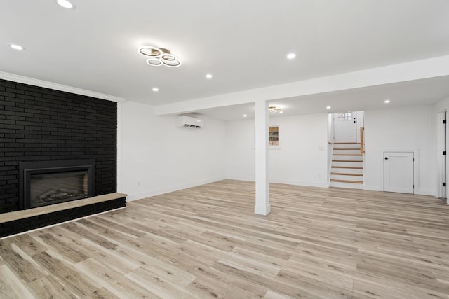 basement featuring light hardwood / wood-style flooring, a wall unit AC, and a brick fireplace