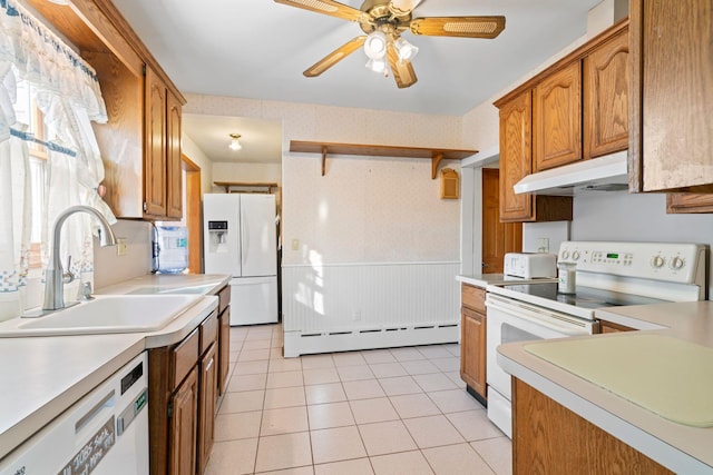 kitchen featuring under cabinet range hood, a wainscoted wall, white appliances, baseboard heating, and wallpapered walls