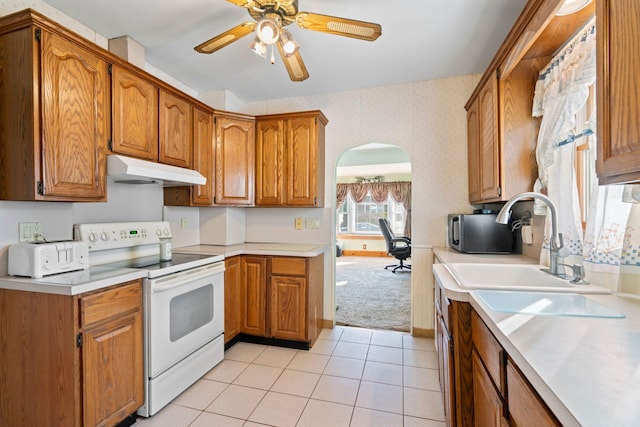 kitchen featuring white electric stove, wallpapered walls, brown cabinetry, and under cabinet range hood