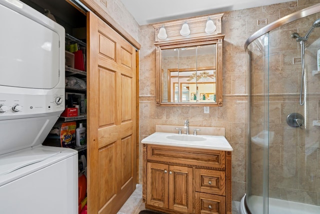 washroom featuring stacked washer and clothes dryer, a sink, tile walls, and laundry area