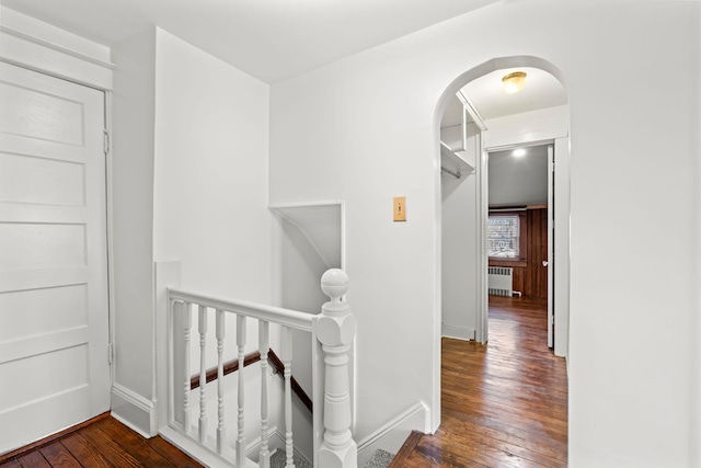 hall featuring arched walkways, baseboards, radiator heating unit, wood-type flooring, and an upstairs landing