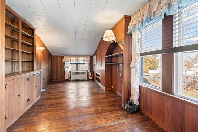 interior space featuring dark wood-style floors, wood walls, radiator heating unit, and built in features