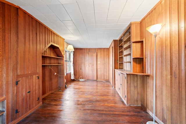 interior space with wood walls, built in shelves, and dark wood finished floors