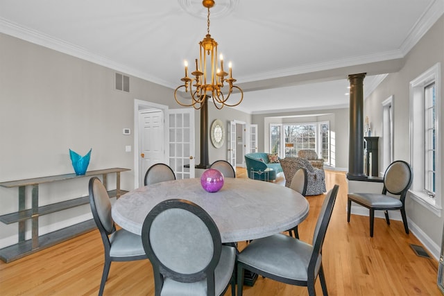 dining room with light wood-type flooring, decorative columns, crown molding, and a notable chandelier