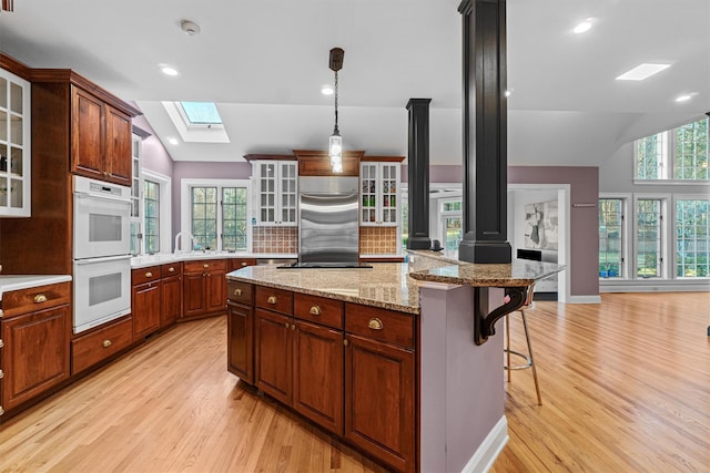 kitchen featuring white double oven, lofted ceiling with skylight, a kitchen island with sink, a kitchen breakfast bar, and light hardwood / wood-style floors