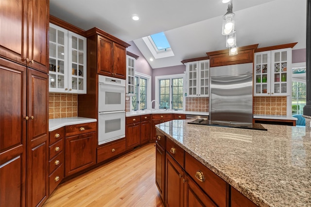 kitchen with white double oven, built in refrigerator, vaulted ceiling with skylight, decorative backsplash, and light wood-type flooring