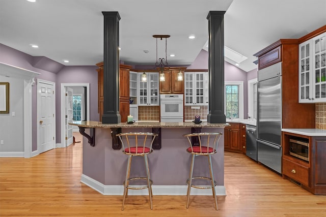 kitchen featuring tasteful backsplash, built in appliances, light hardwood / wood-style flooring, and a kitchen bar