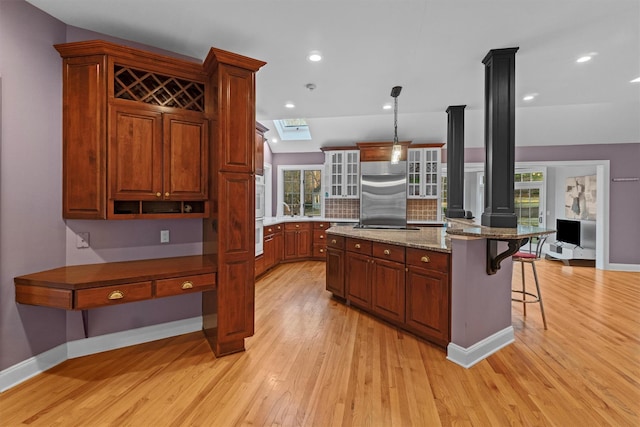 kitchen featuring a kitchen island, decorative light fixtures, light hardwood / wood-style floors, stainless steel built in refrigerator, and a breakfast bar area