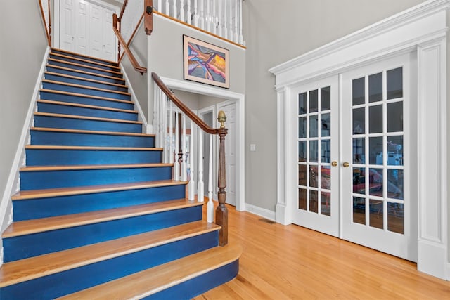 stairway with french doors, a high ceiling, and hardwood / wood-style floors