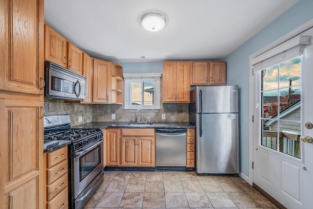 kitchen with stainless steel appliances, sink, decorative backsplash, and dark stone counters