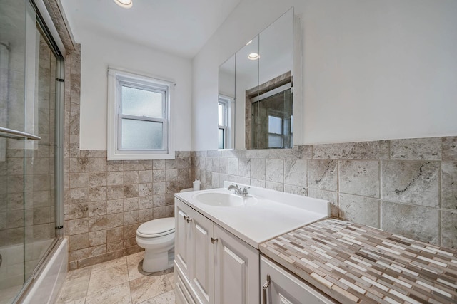 full bathroom featuring vanity, tile walls, shower / bath combination with glass door, and toilet