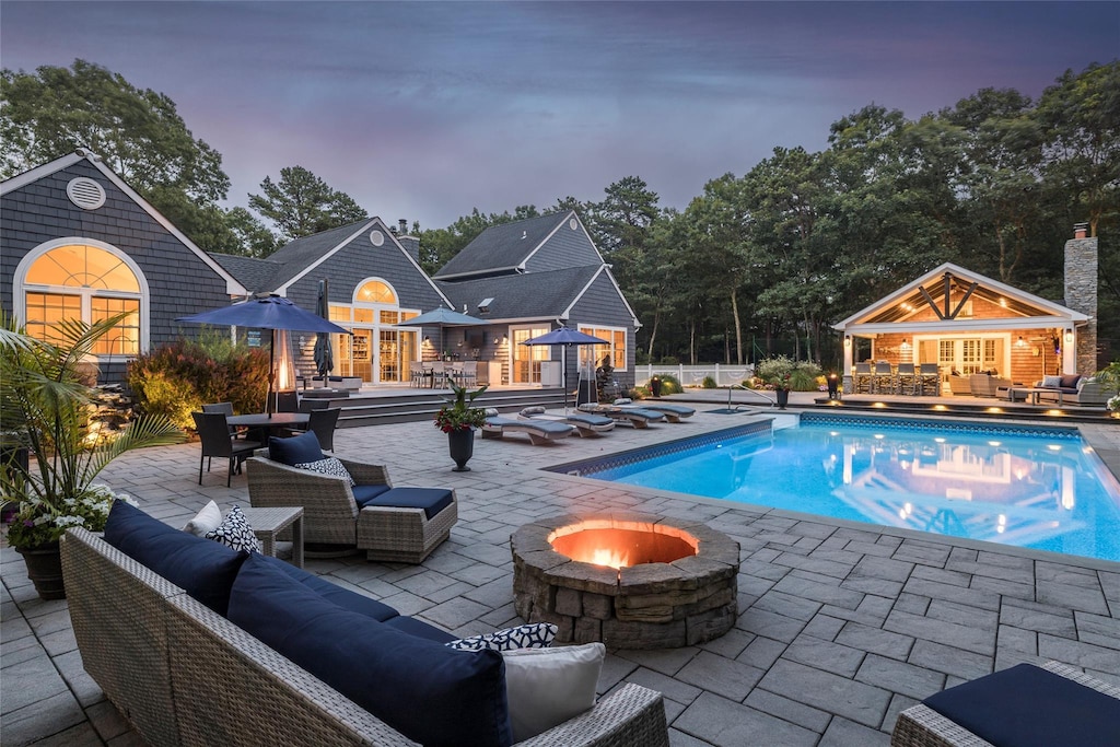 pool at dusk with an outdoor structure, a patio, and an outdoor living space with a fire pit