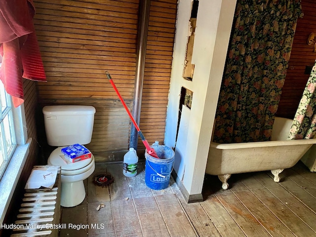 bathroom featuring wood-type flooring, toilet, a bathtub, and wooden walls