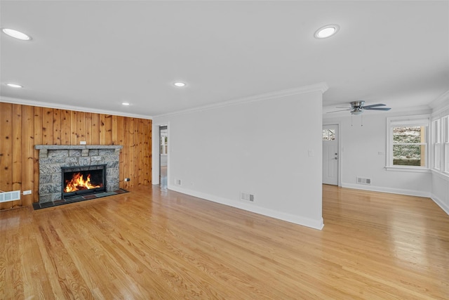 unfurnished living room featuring light hardwood / wood-style flooring, a stone fireplace, ceiling fan, and ornamental molding