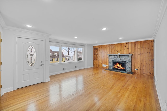 unfurnished living room featuring wood walls, light hardwood / wood-style floors, ornamental molding, and a fireplace